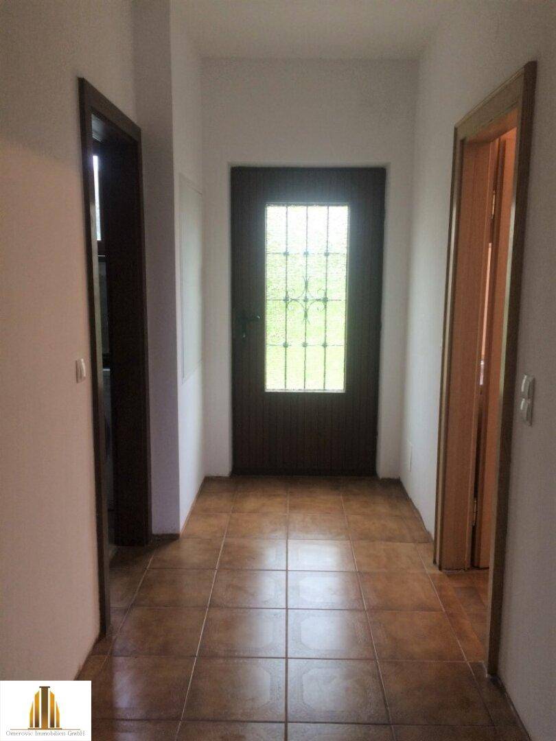 Heller Eingangsbereich mit braunen Fliesen und einer Holztür mit Glaseinsätzen.