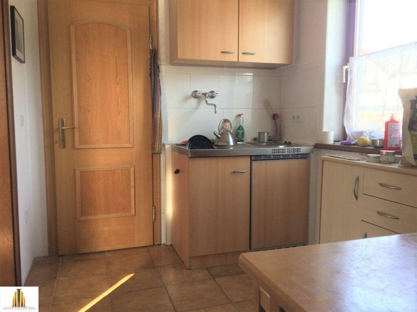 Kleine Küche mit Fliesenboden, einfacher Küchenzeile und Fenster mit Tageslicht.