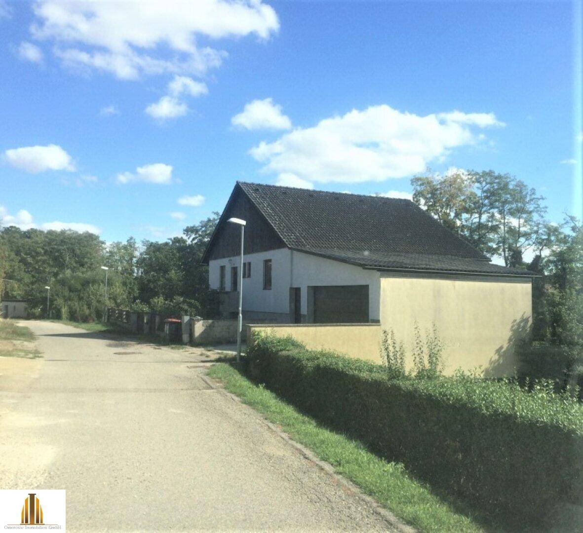 Seitenansicht des Hauses mit Garage und Zufahrt, umgeben von Bäumen und Hecken.