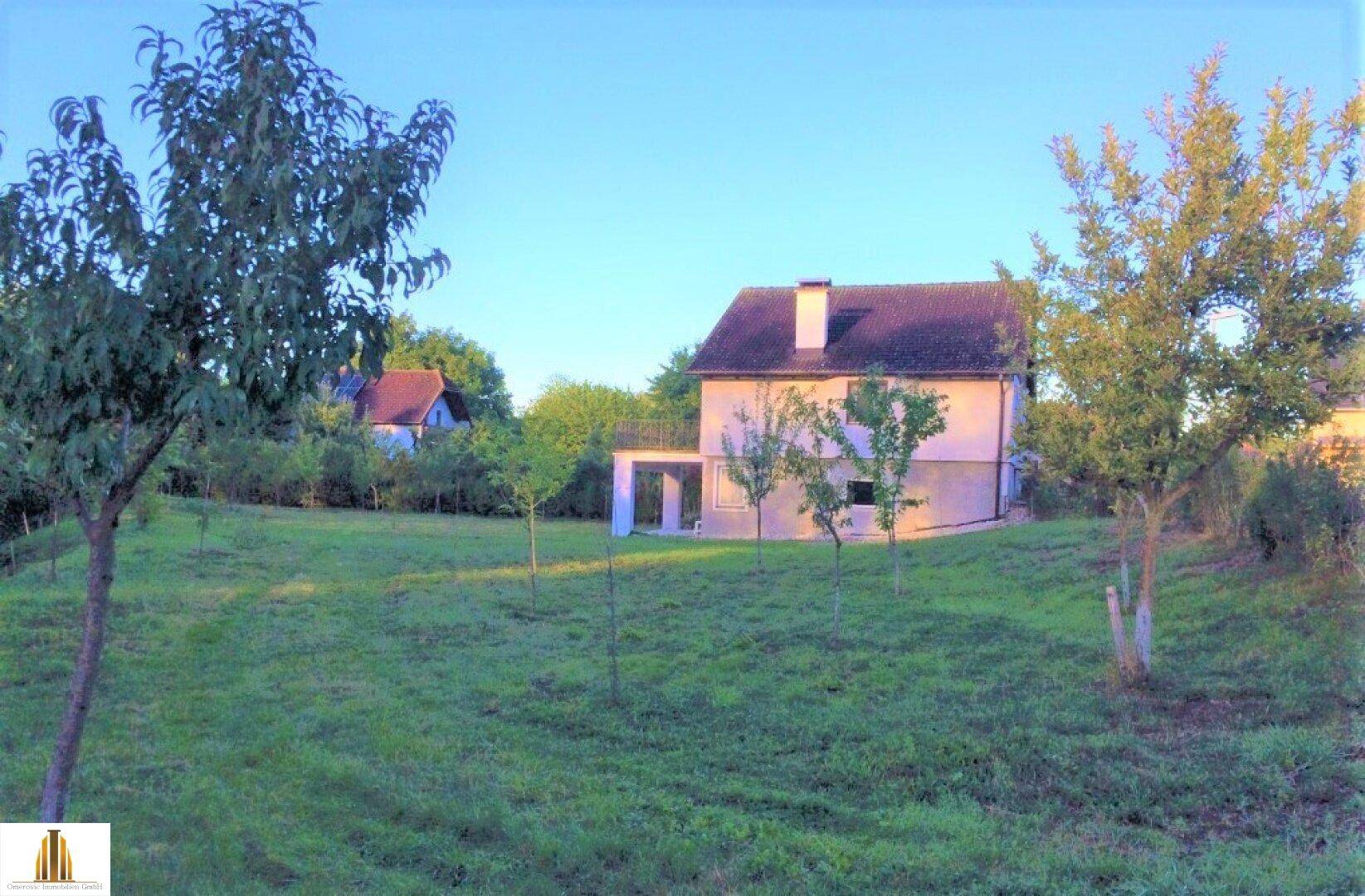 Haus in ländlicher Umgebung mit großem Garten und jungen Obstbäumen.