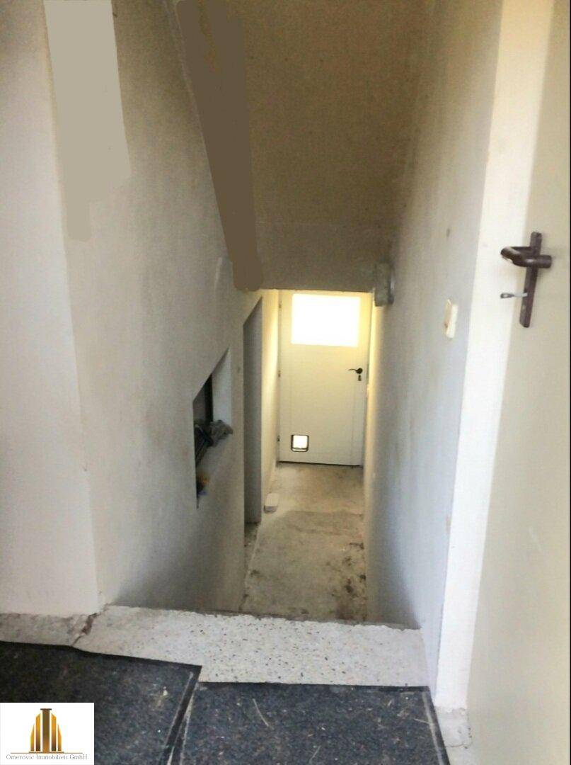 Treppenabgang in den Kellerbereich mit einfacher Ausstattung und Tür am Ende.