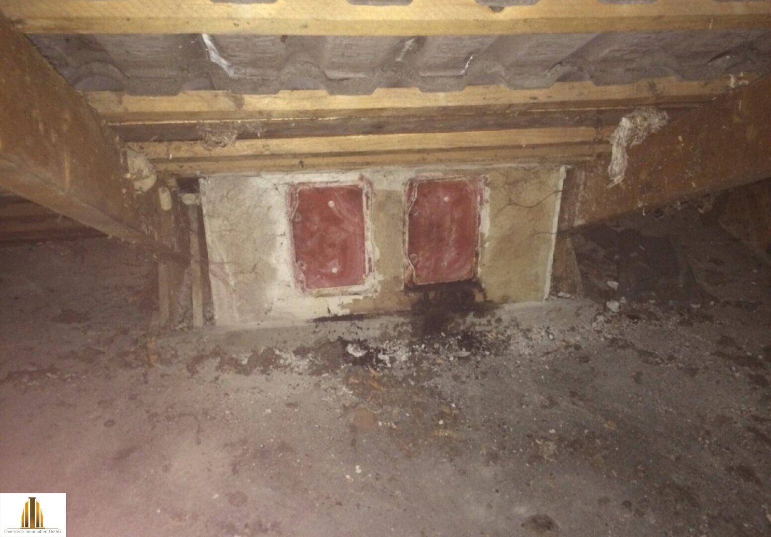 Dachbodenbereich mit Holzbalken und zwei verschlossenen Öffnungen in der Wand.