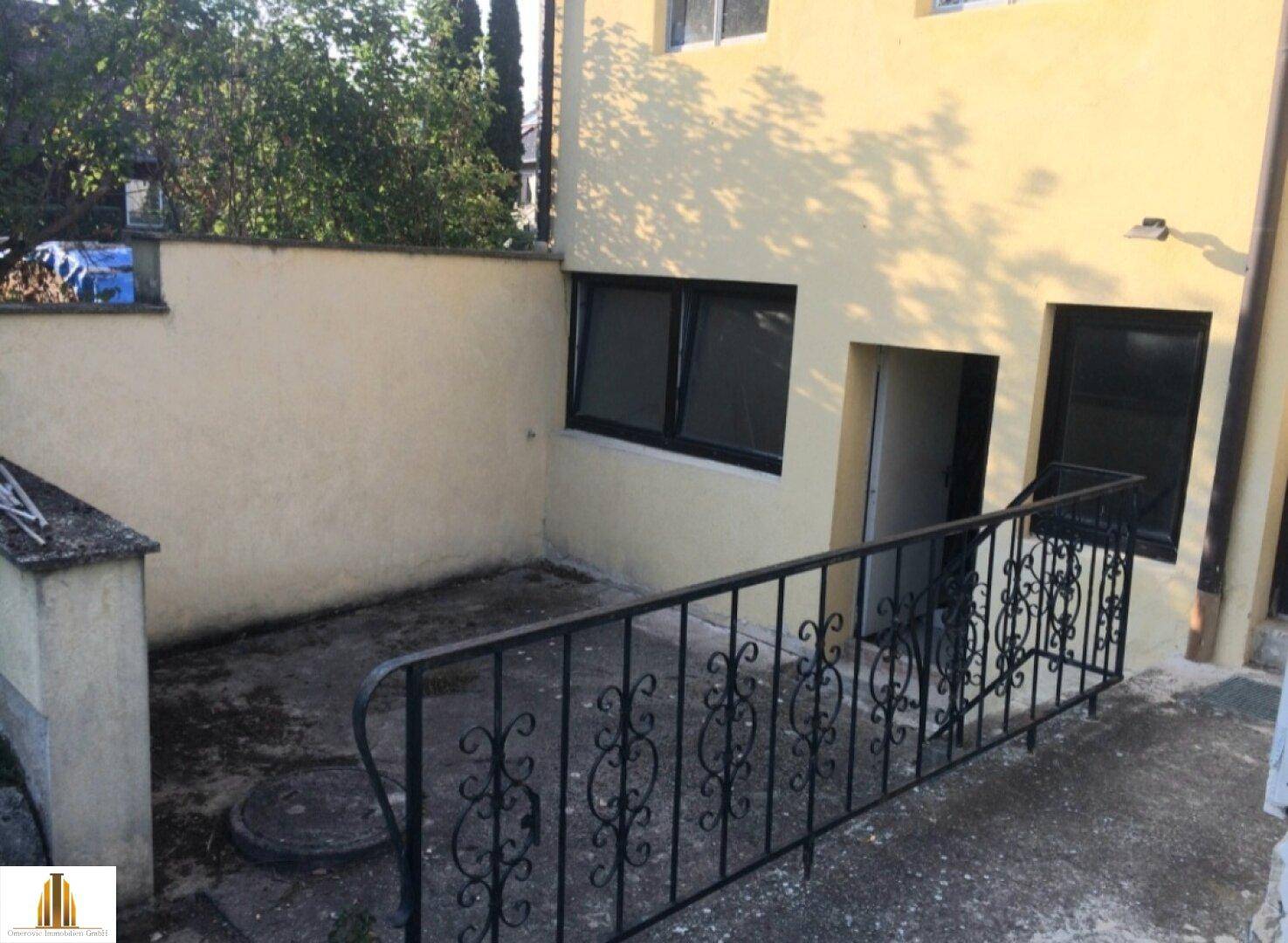 Kleiner gepflasterter Bereich neben dem Haus mit Geländer und Zugang zum Keller.