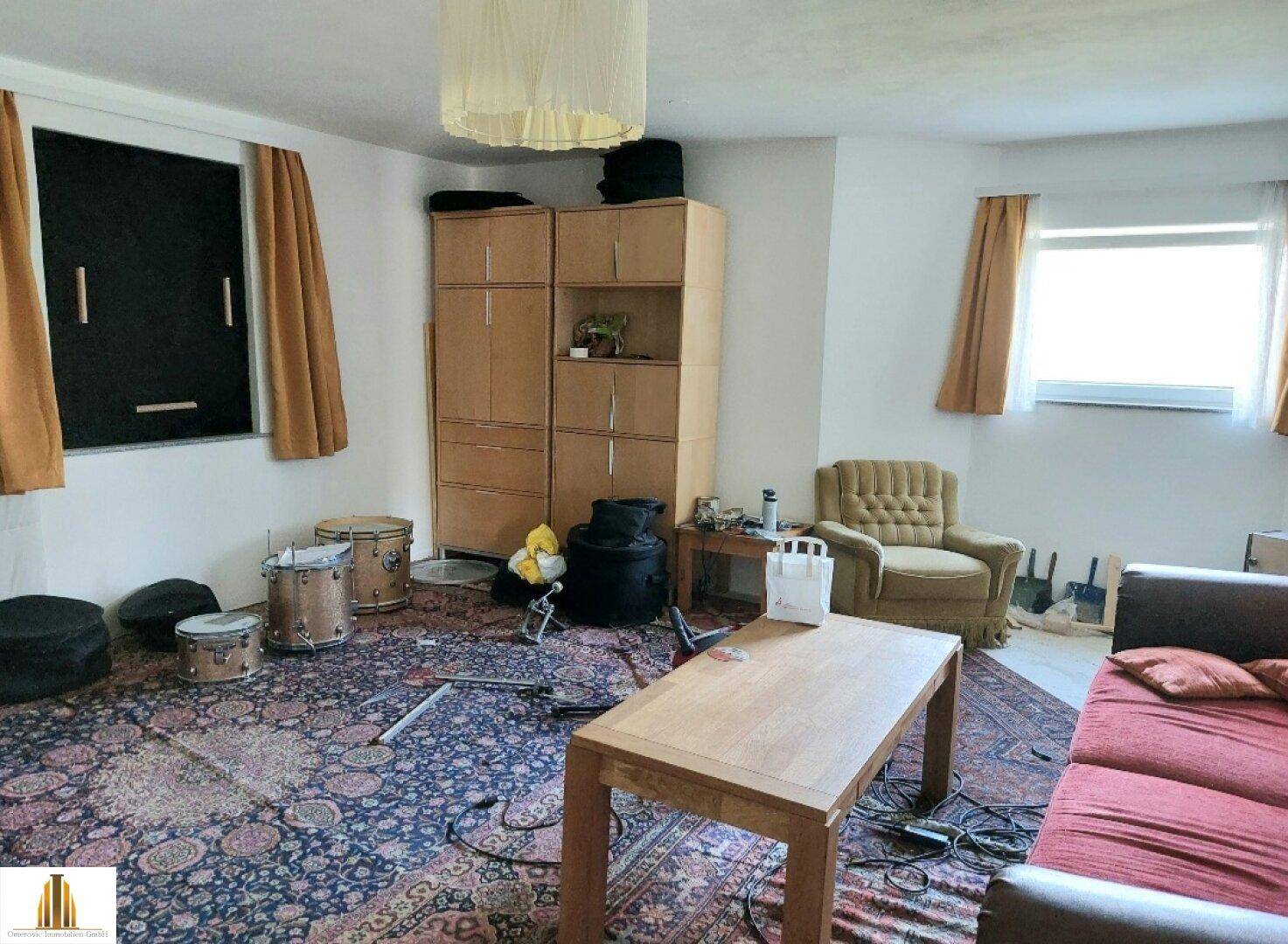 Geräumiges Wohnzimmer mit Teppichboden, Möbeln und einem Schlagzeug-Set.