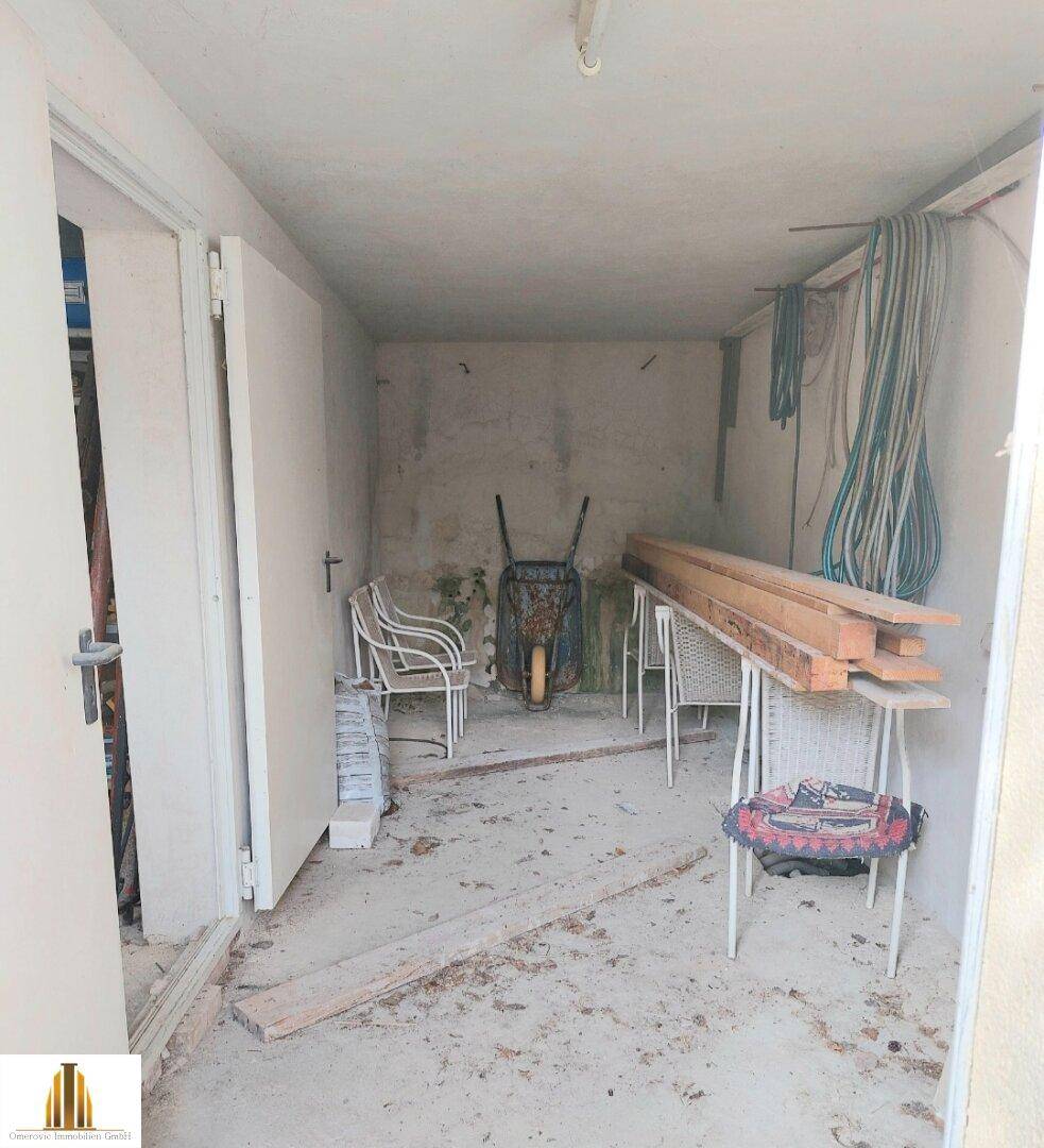 Einfacher Abstellraum mit Betonboden, Gartengeräten und Baumaterialien.