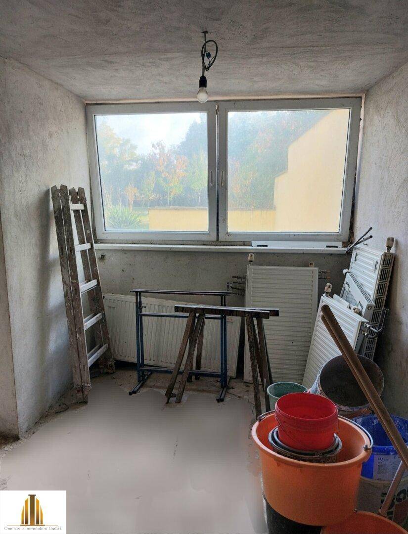Raum in Renovierung mit großem Fenster, Heizkörpern und Baueimern.
