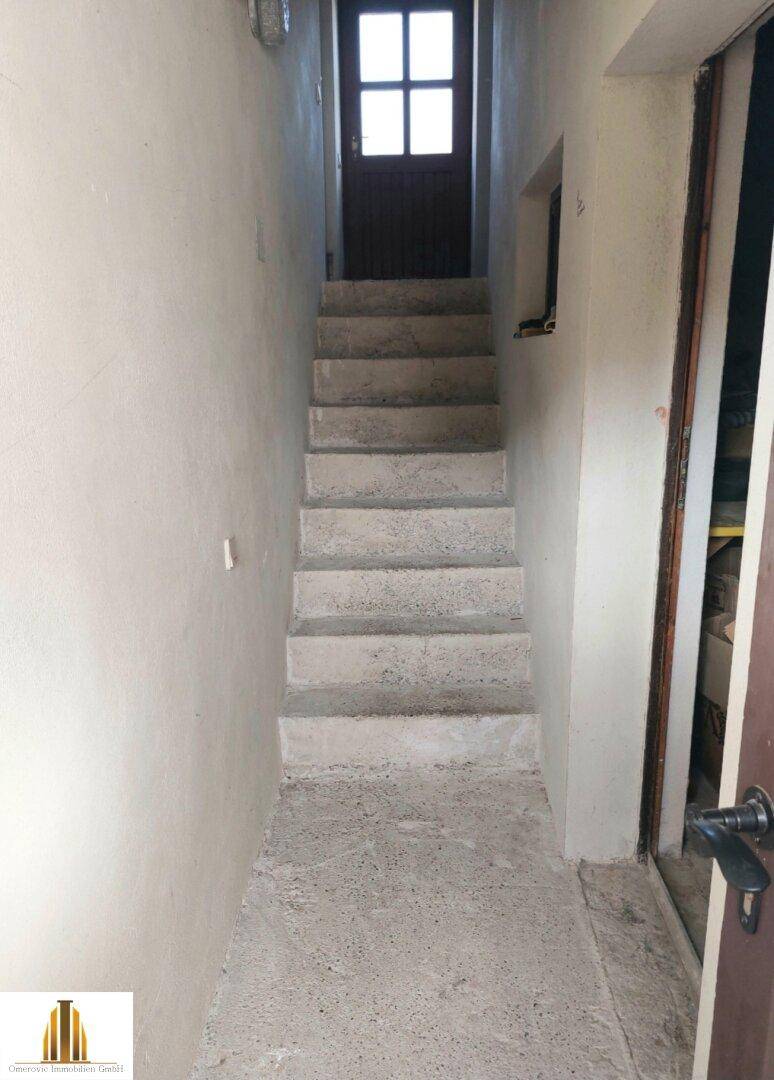 Treppenaufgang in einem Flur mit einfacher Gestaltung und einer Holztür am oberen Ende.