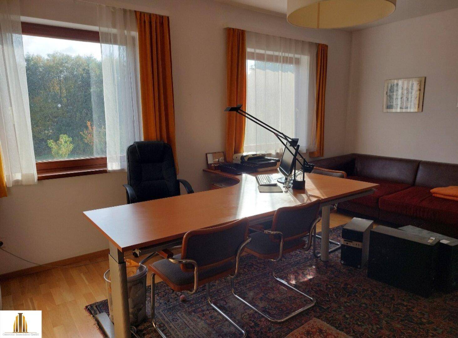 Geräumiges Büro mit Holzboden, großem Schreibtisch und Blick ins Grüne durch die Fenster.