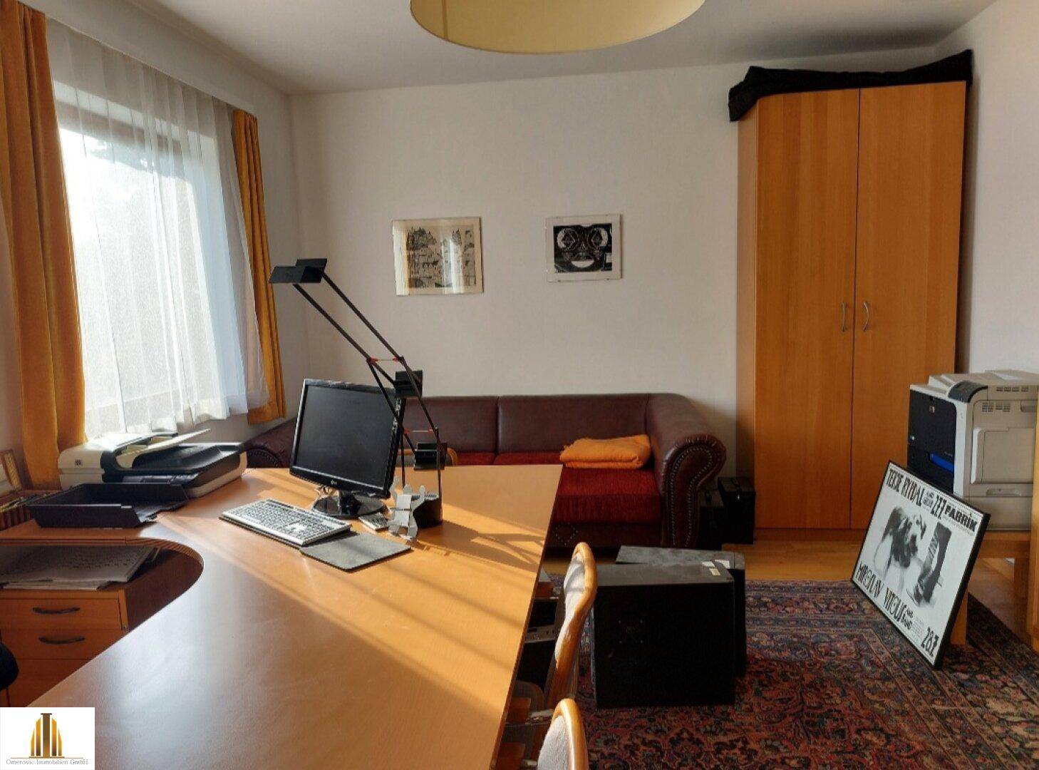 Arbeitszimmer mit Schreibtisch, Sofa und einem großen Kleiderschrank aus hellem Holz.