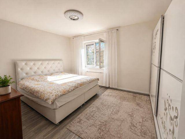 Helles Schlafzimmer mit gepolstertem Bett, Kleiderschrank und Teppichboden.