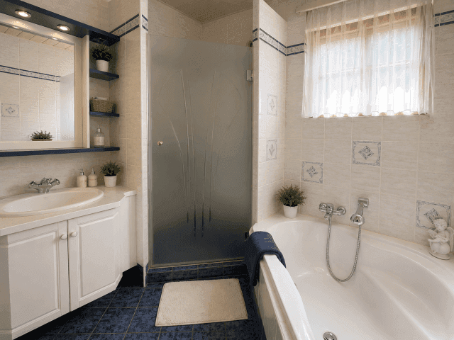 Badezimmer mit Badewanne, Duschkabine und Fenster, in hellen und blauen Fliesen gehalten.