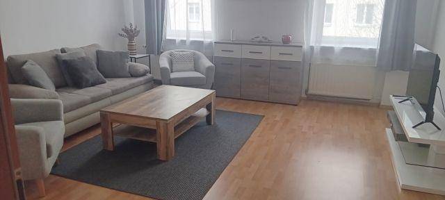 Helles Wohnzimmer mit modernem Sofa, Holzboden und großen Fenstern.