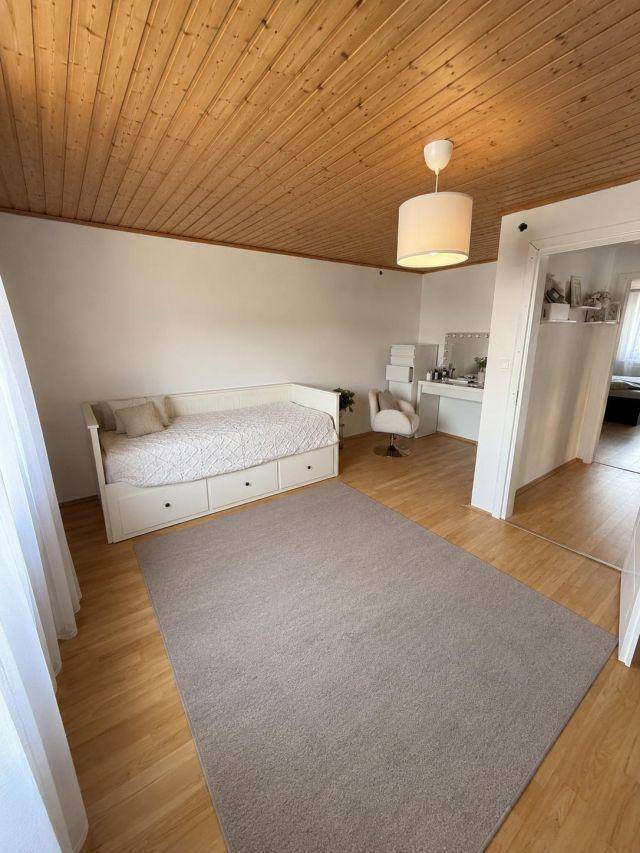 Helles Schlafzimmer mit Holzbalkendecke, Tagesbett und Schreibtischbereich.