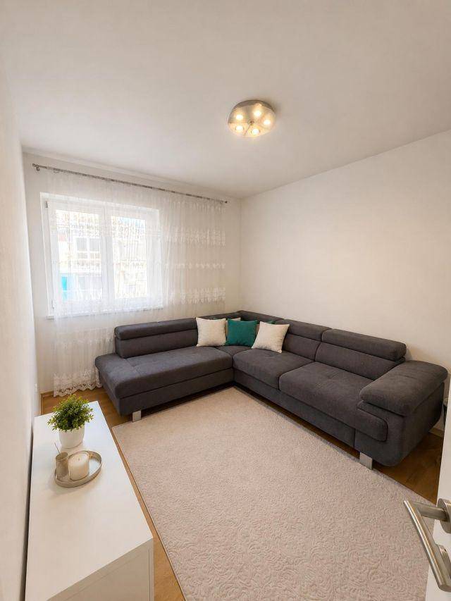Gemütliches Wohnzimmer mit Ecksofa, Teppich und Fenster mit Vorhängen.