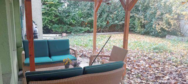 Gemütlicher Außenbereich unter einer Holzpergola mit Gartenmöbeln und Blick ins Grüne.