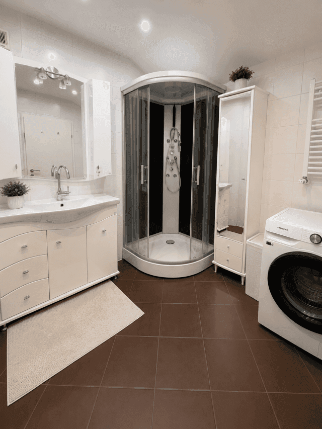 Modernes Badezimmer mit Duschkabine, Waschmaschine, weißem Waschtisch und Fliesenboden.