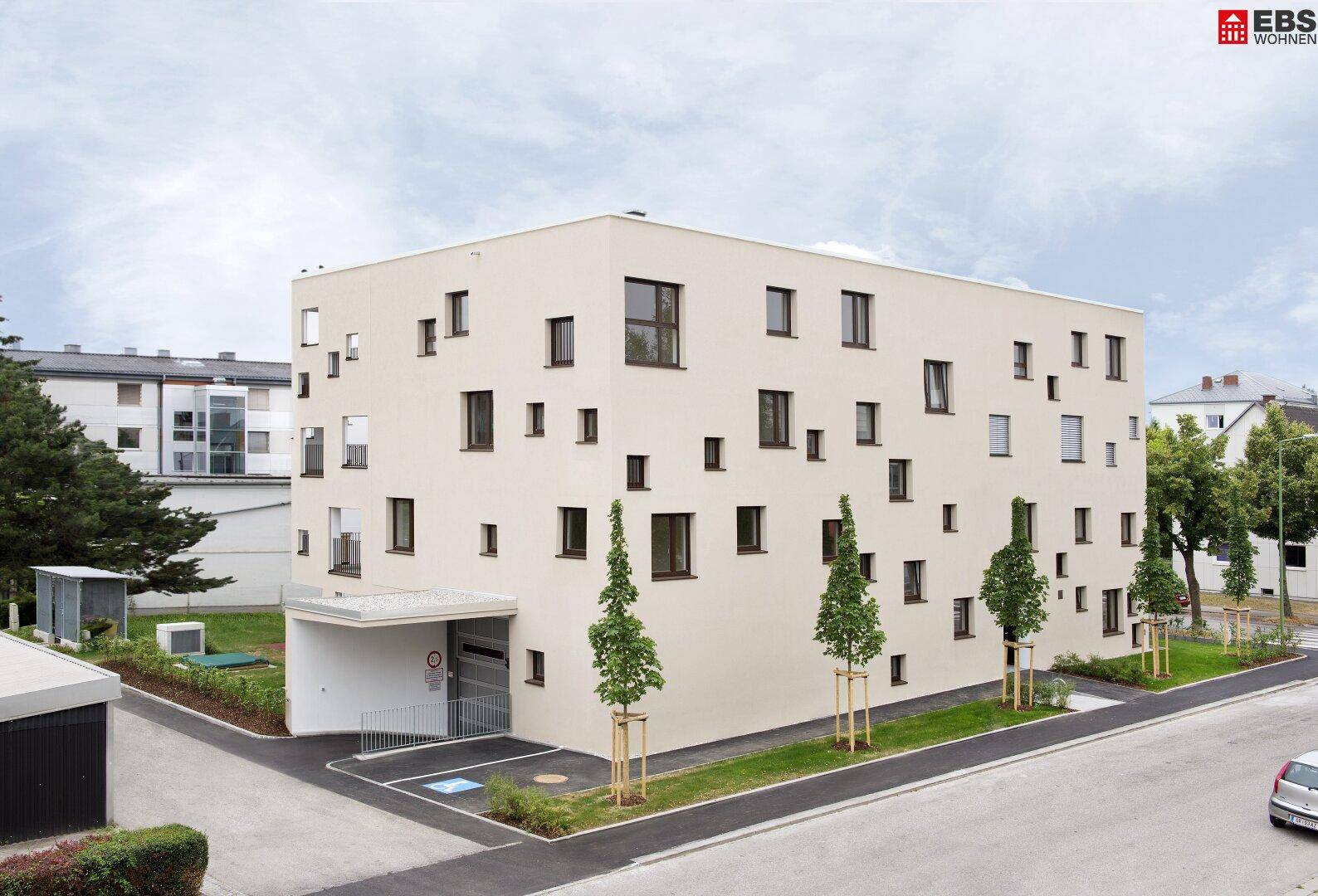 Ansicht des modernen Wohngebäudes mit Zufahrt zur Tiefgarage und gepflegter Grünanlage.