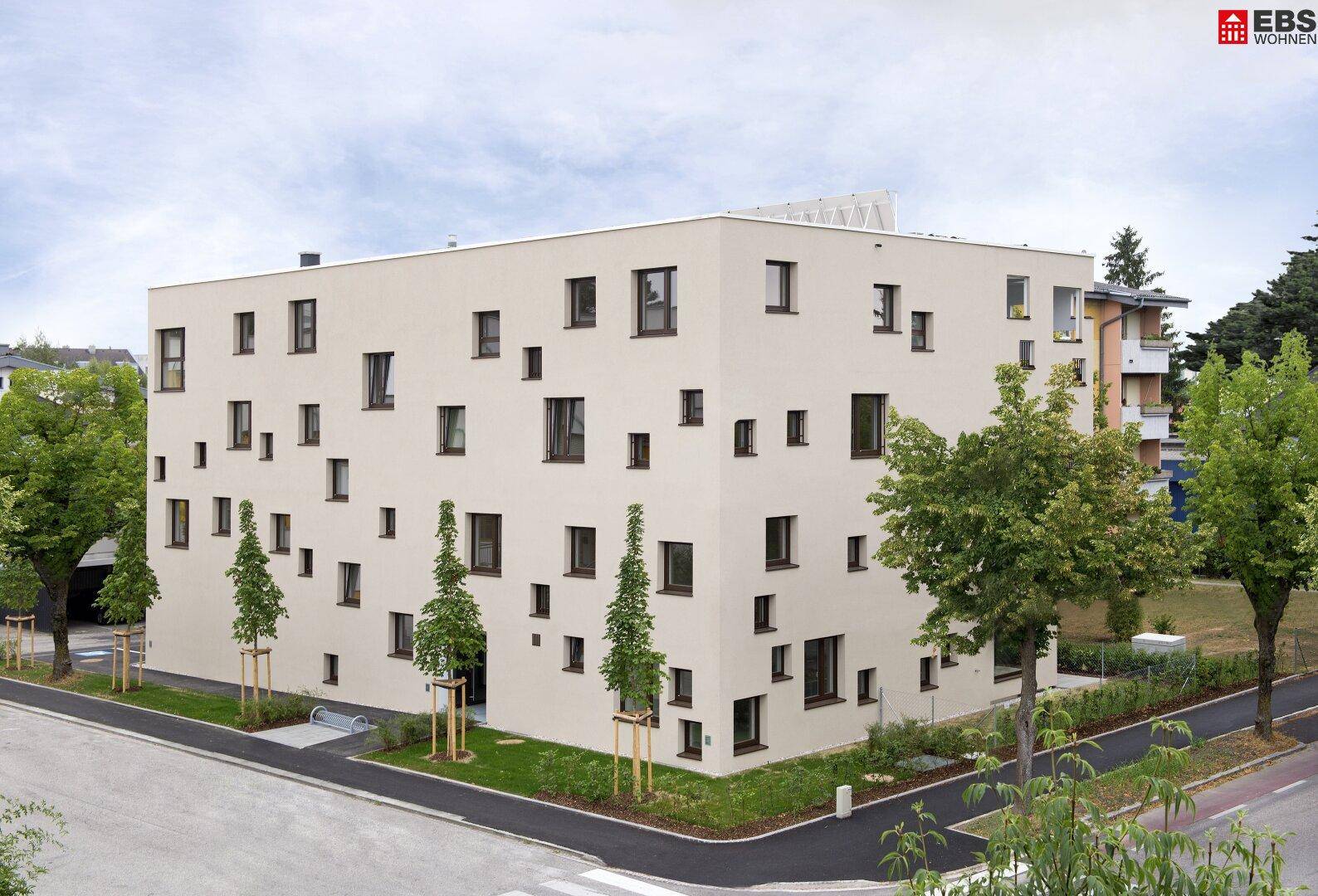 Modernes Mehrfamilienhaus mit heller Fassade und unregelmäßig angeordneten Fenstern.