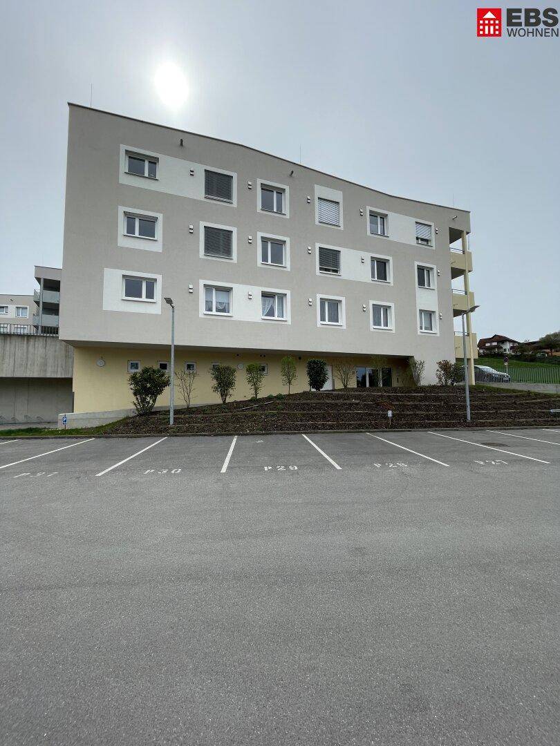 Modernes Mehrfamilienhaus mit heller Fassade und Parkplätzen davor.