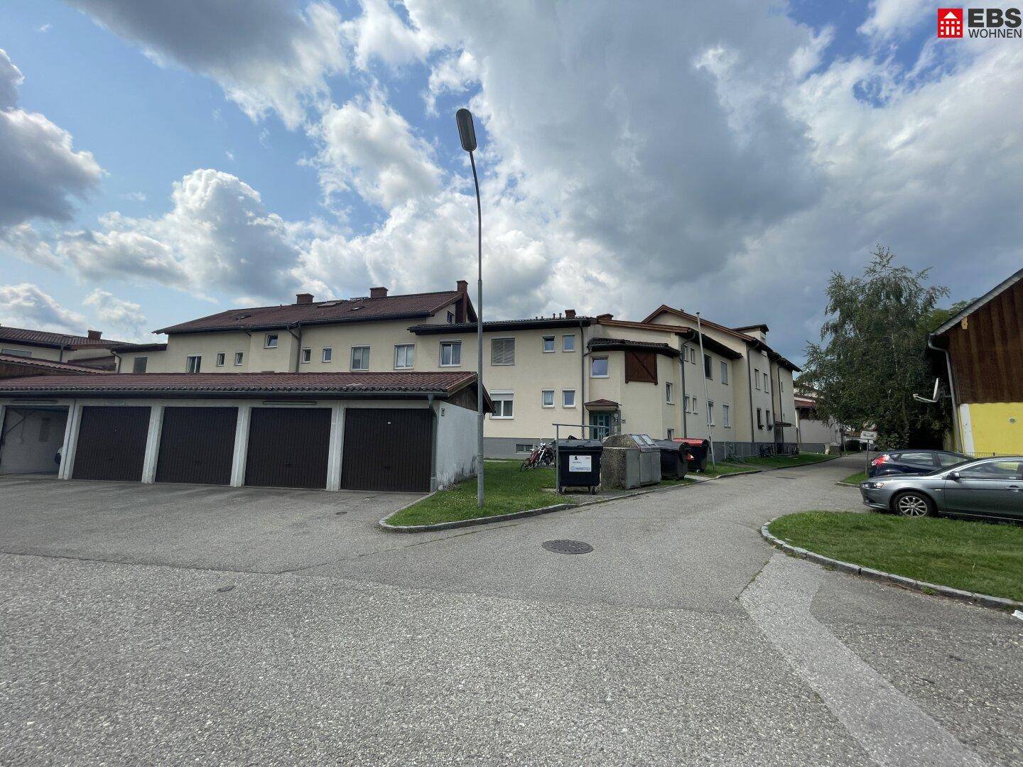 Mehrfamilienhaus mit Garagen und Parkplätzen unter bewölktem Himmel.