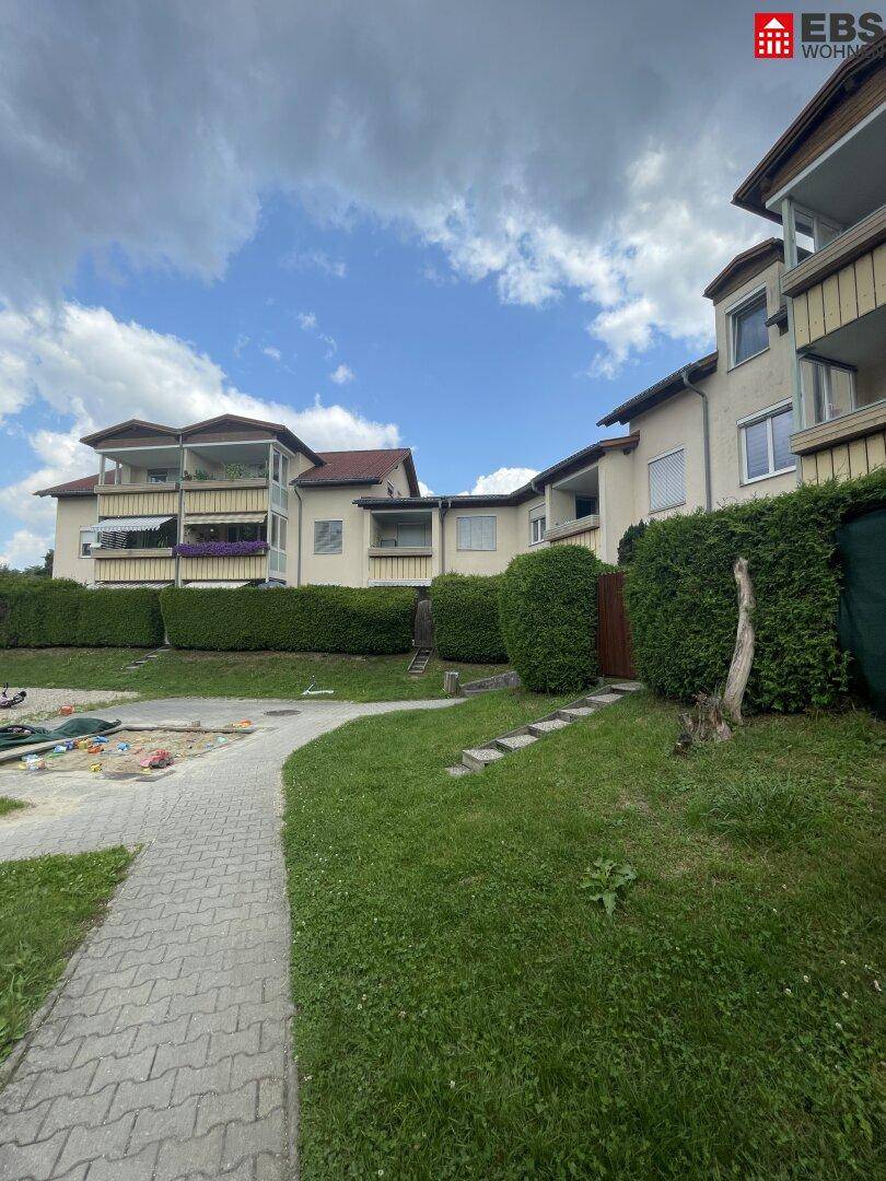 Wohngebäude mit Balkonen, gepflegtem Rasen, Hecken und einem Kinderspielplatz.