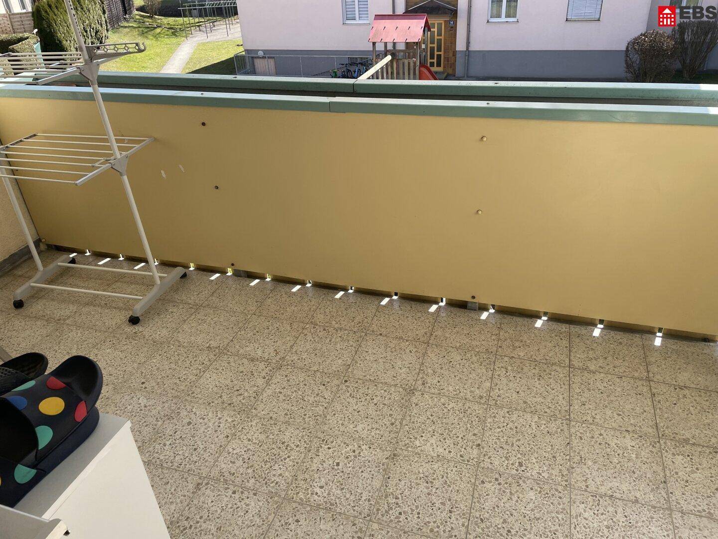 Balkon mit Fliesenboden und Blick auf einen Spielplatz und die umliegenden Gebäude.