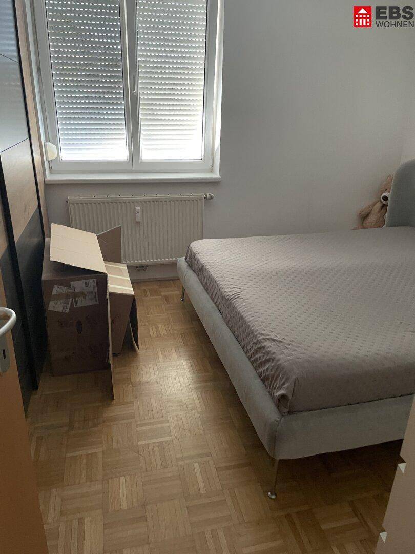 Schlafzimmer mit Bett, Kleiderschrank und Fenster mit Rollläden, ausgestattet mit Parkettboden.