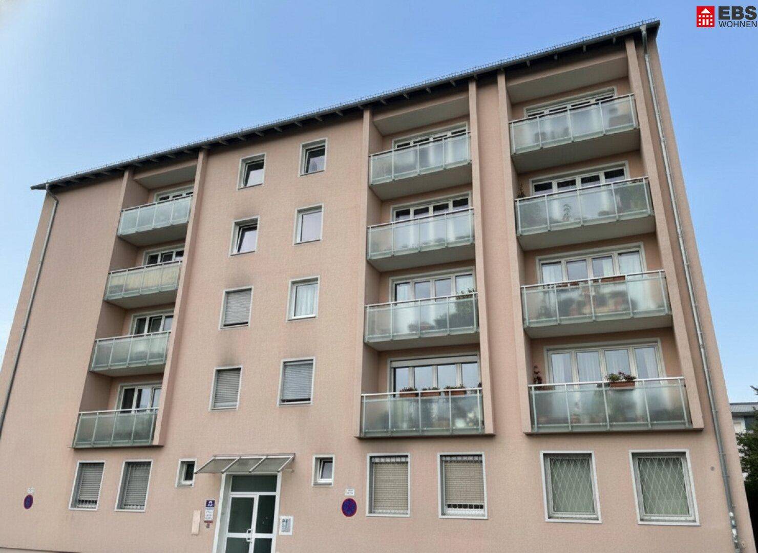 Mehrfamilienhaus mit mehreren Balkonen und moderner Fassadengestaltung unter klarem Himmel.