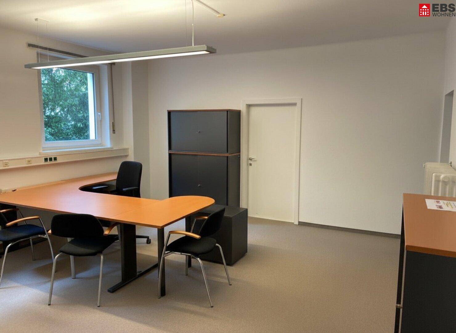 Funktional eingerichtetes Büro mit Schreibtisch, Besprechungstisch und heller Beleuchtung.