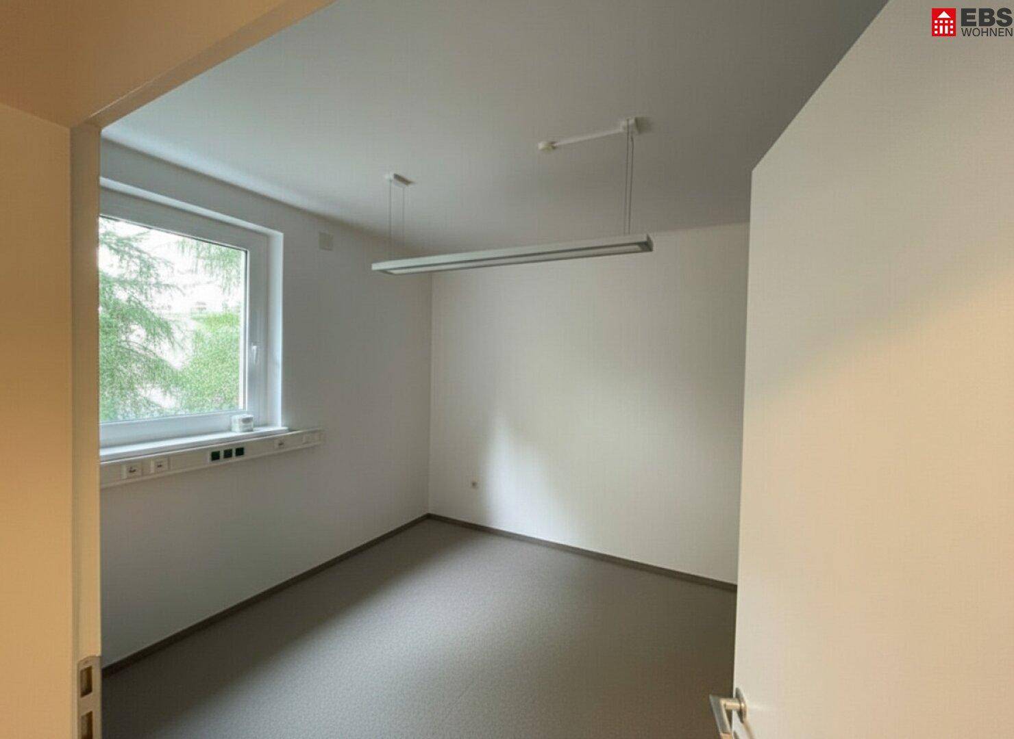 Kleineres Büro mit Teppichboden, einem Fenster und einfacher Deckenbeleuchtung.