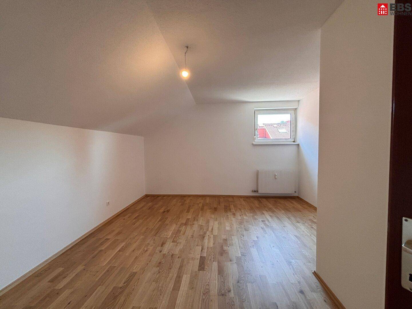 Freundliches Zimmer im Dachgeschoss mit Holzboden und einem Fenster, das Tageslicht hereinlässt.