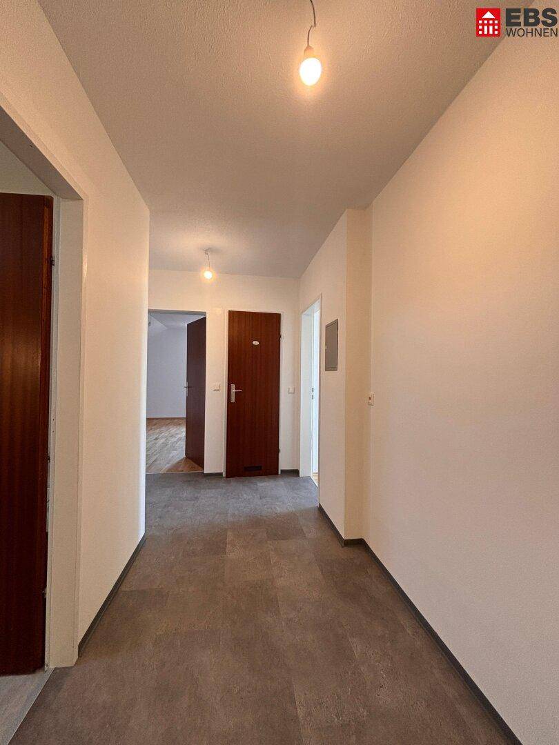 Langer Flur mit dunklem Fliesenboden, der zu weiteren Räumen der Wohnung führt.