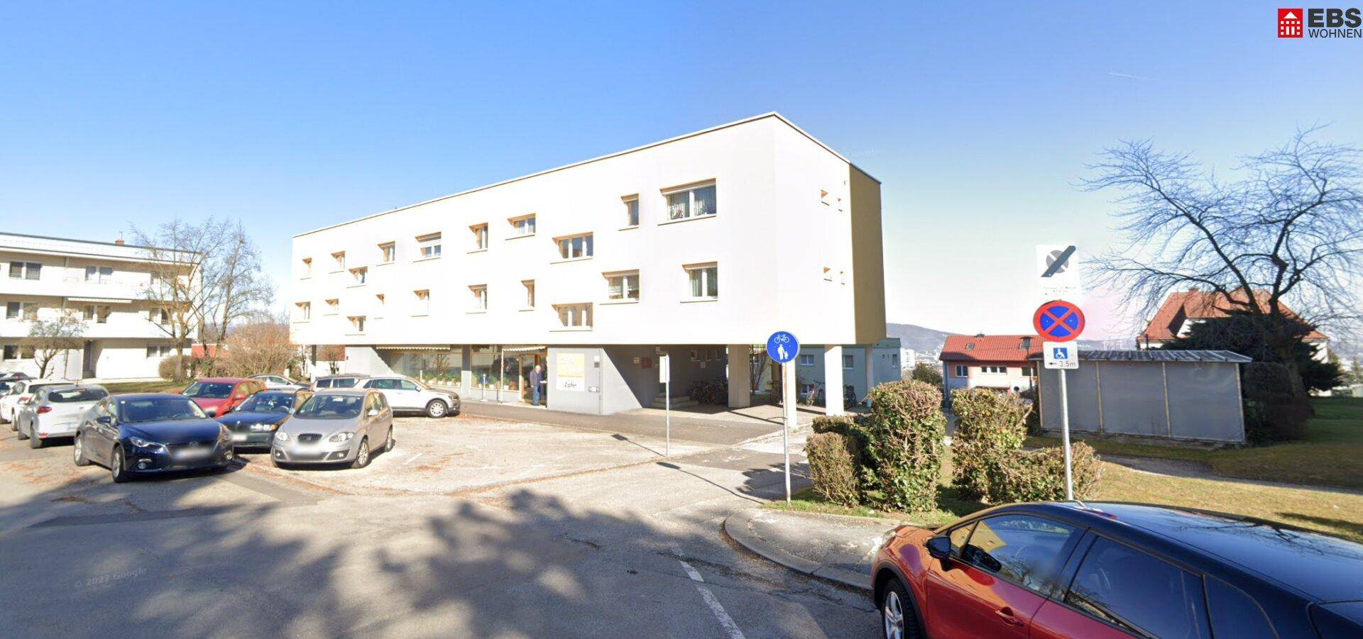 Gebäudeansicht von der Straße aus mit parkenden Fahrzeugen und umliegender Wohnbebauung.