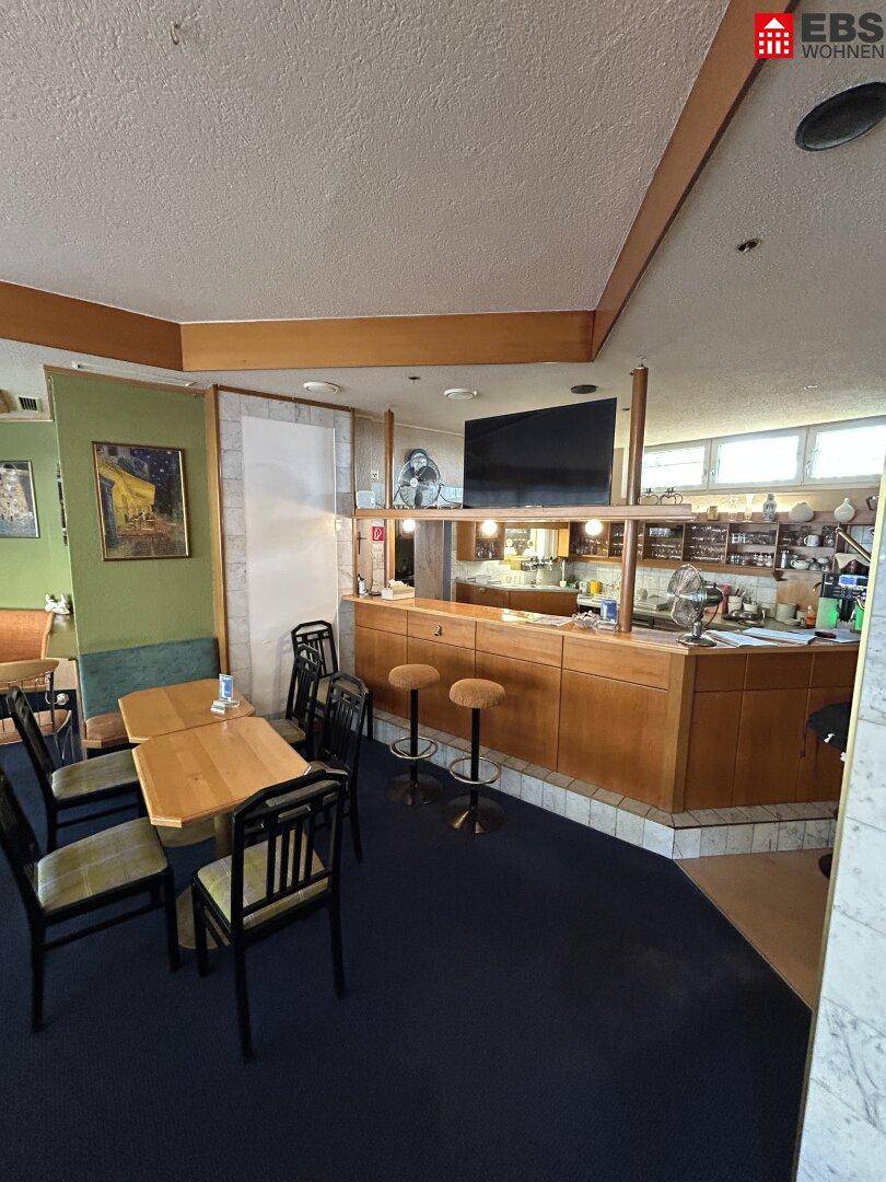 Innenbereich eines Cafés mit Sitzgelegenheiten, einer Bar und einem Fernseher an der Wand.