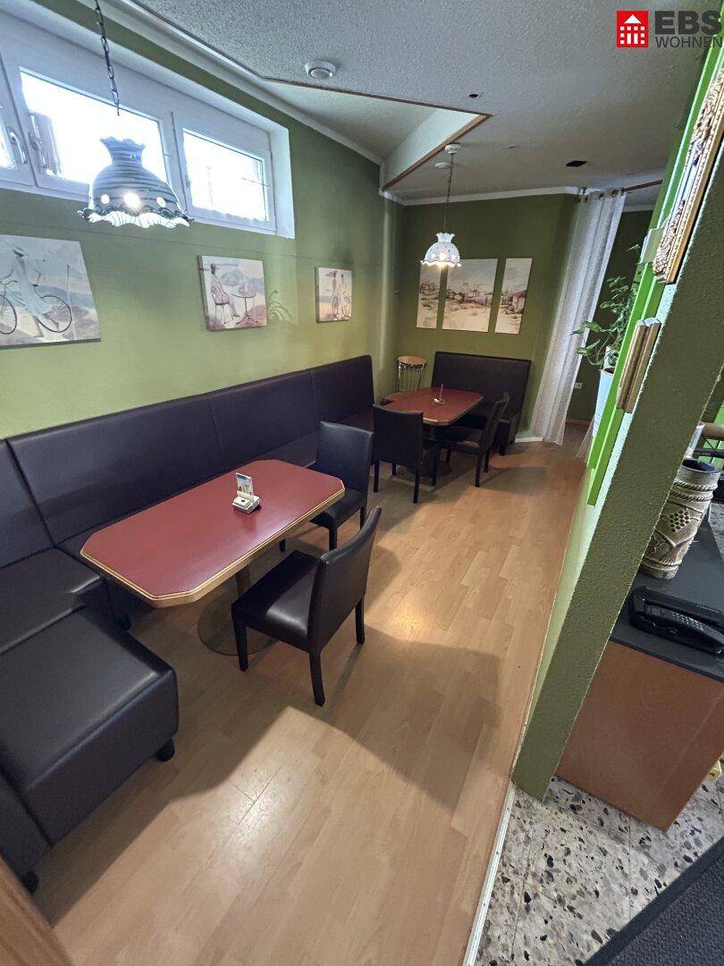 Gemütlicher Sitzbereich im Café mit Holzboden, gepolsterten Bänken und kleinen Tischen.