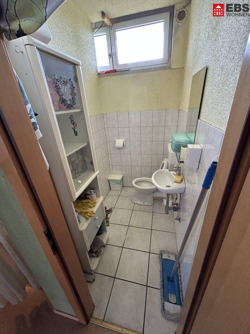 Kleine Toilette mit Waschbecken, WC und einem Fenster für natürliche Belüftung.