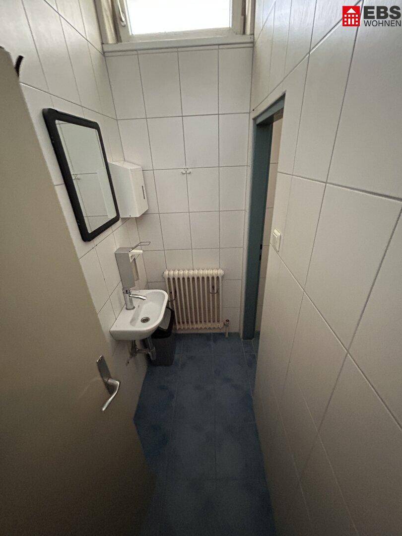 Schmale Toilette mit Waschbecken, Heizkörper und einem Fenster für Tageslicht.