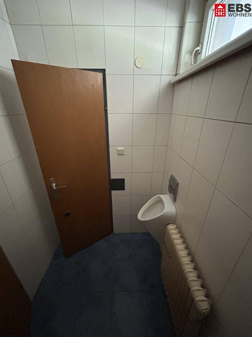 Toilette mit Urinal, Heizkörper und einem Fenster für natürliche Belichtung.