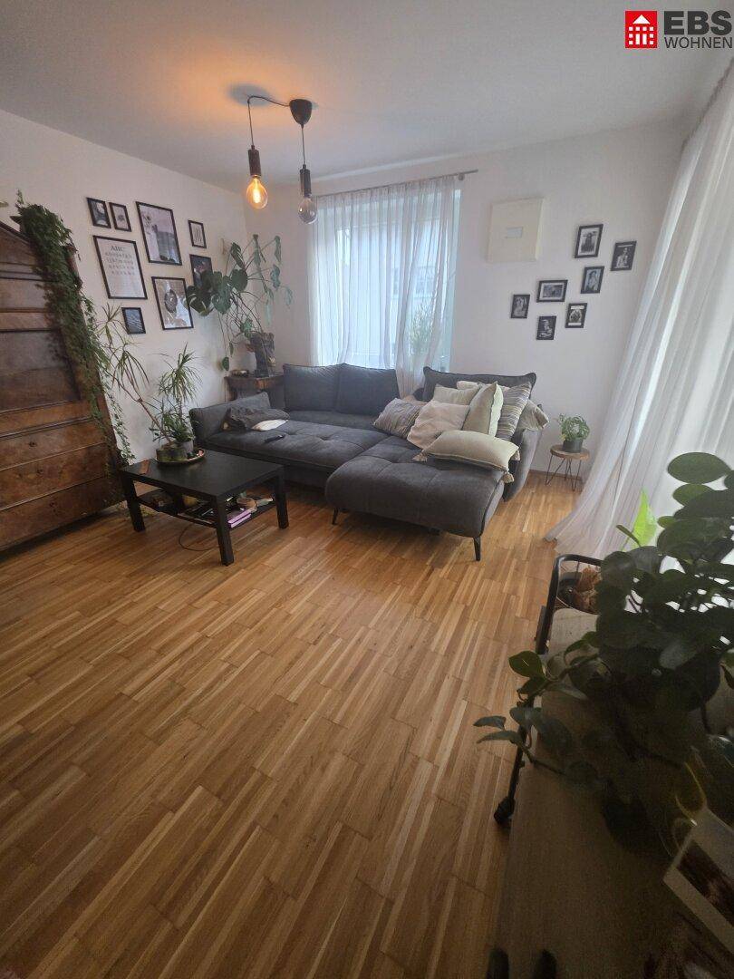 Gemütliches Wohnzimmer mit großem Ecksofa, Holzboden und vielen Pflanzen.