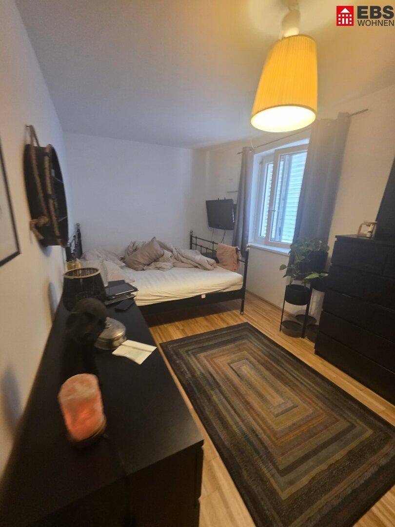 Schlafzimmer mit Doppelbett, Holzboden und einem Fenster mit Jalousien.