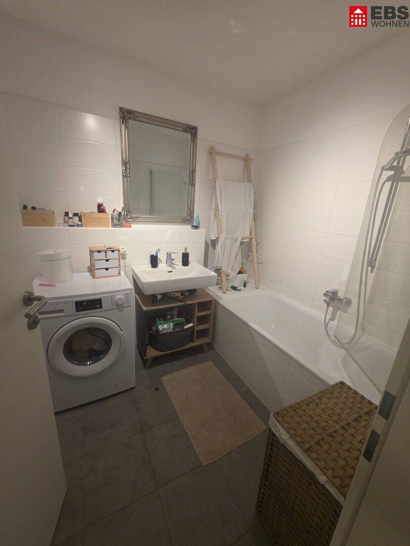 Badezimmer mit Badewanne, Waschbecken, Waschmaschine und weißen Fliesen.