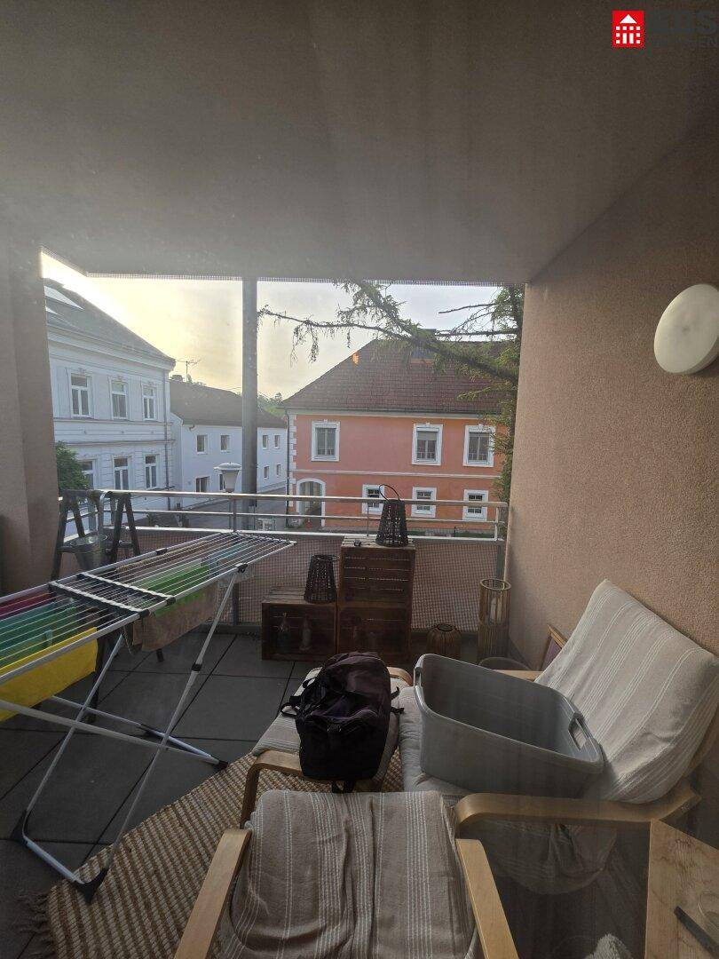 Überdachter Balkon mit Wäscheständer, Sitzgelegenheiten und Blick auf umliegende Gebäude.