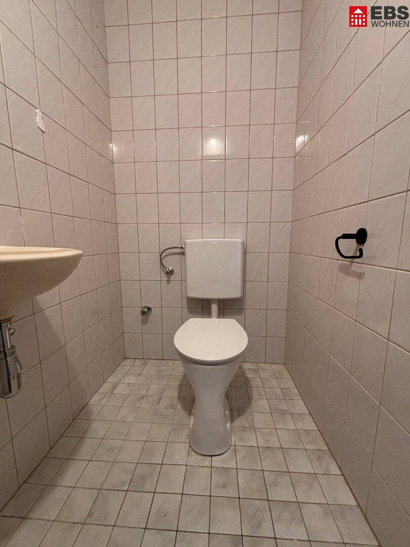 Einfaches separates WC mit weißen Fliesen und Toilette.