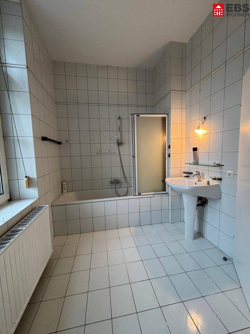 Badezimmer mit weißen Fliesen, Badewanne und Duschabtrennung.