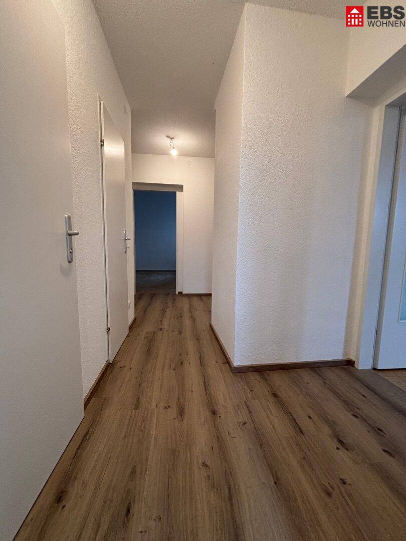 Langer, heller Flur mit Laminatboden und weißen Wänden, der zu weiteren Räumen führt.