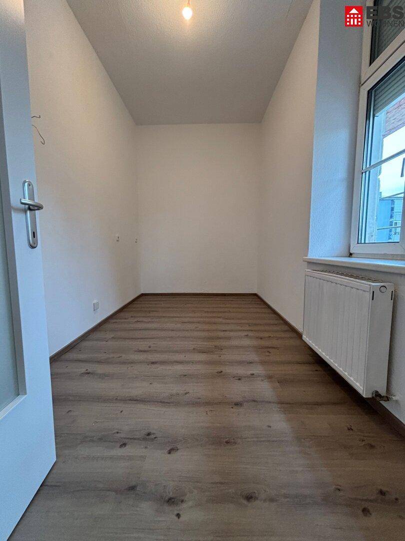 Leerer Raum mit Laminatboden und Fenster, bereit zur individuellen Gestaltung.