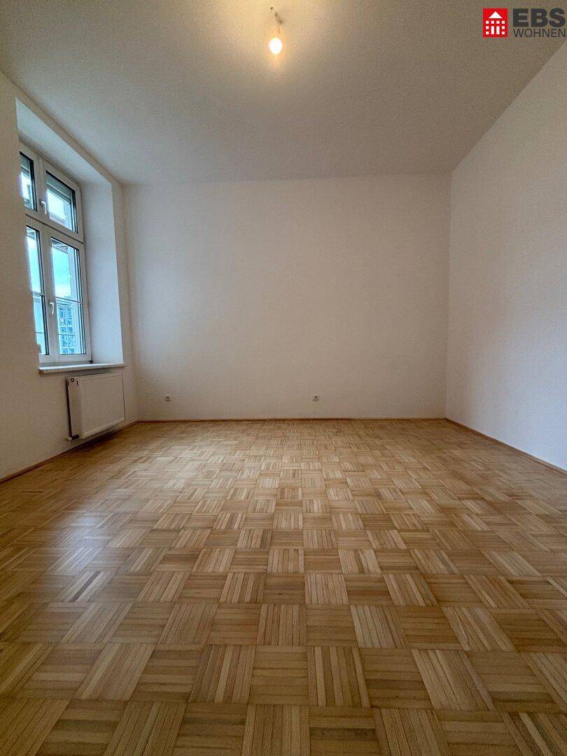 Leeres Schlafzimmer mit Parkettboden und großem Fenster, ideal für individuelle Einrichtung.