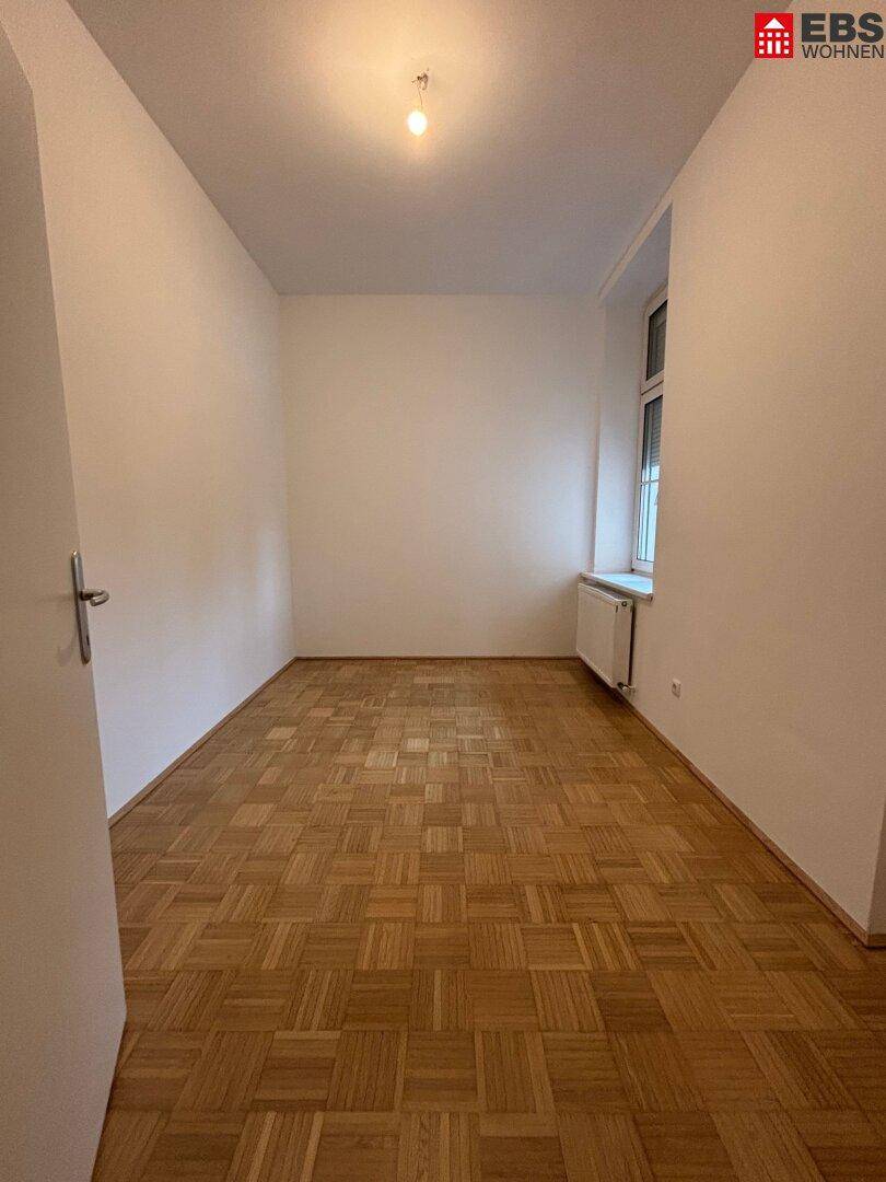 Heller, leerer Raum mit Parkettboden und Fenster, vielseitig nutzbar.