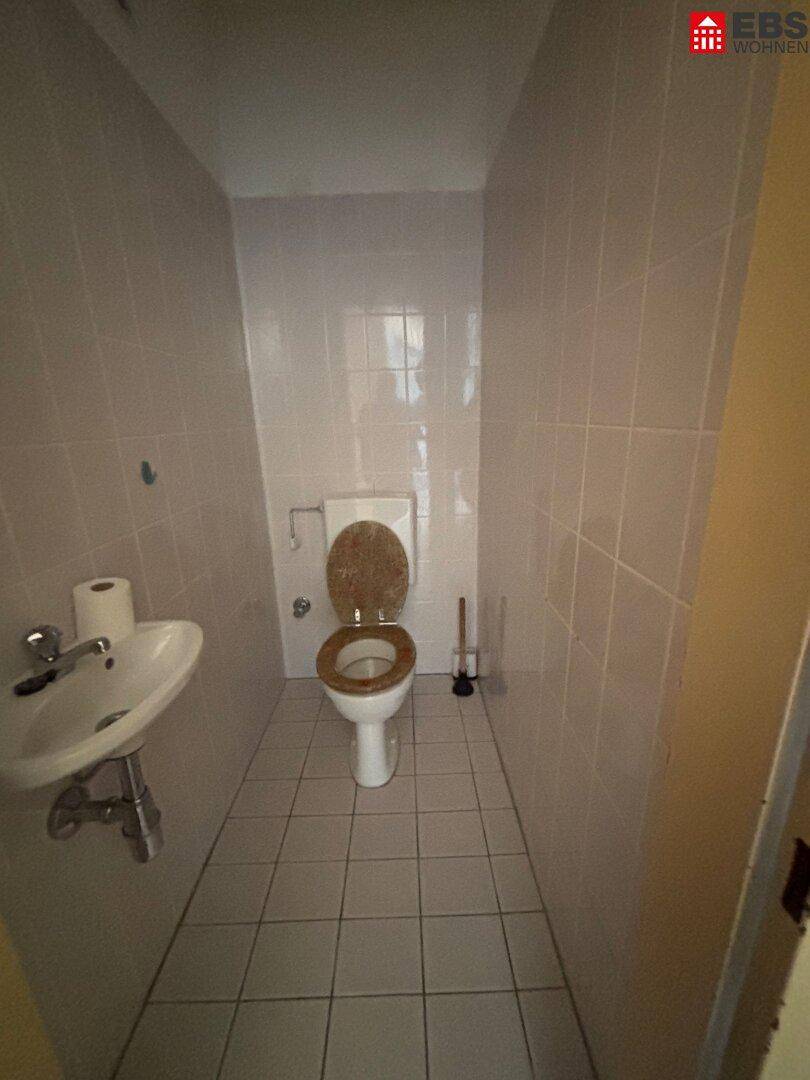 Kleines separates WC mit Toilette, Waschbecken und hellen Fliesen an Wänden und Boden.