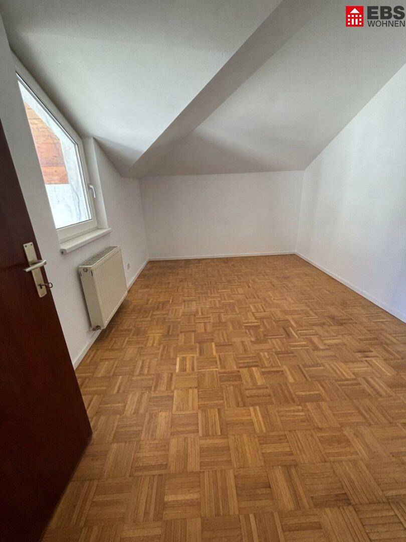 Leeres Zimmer im Dachgeschoss mit Parkettboden und Fenster, bereit zur individuellen Gestaltung.
